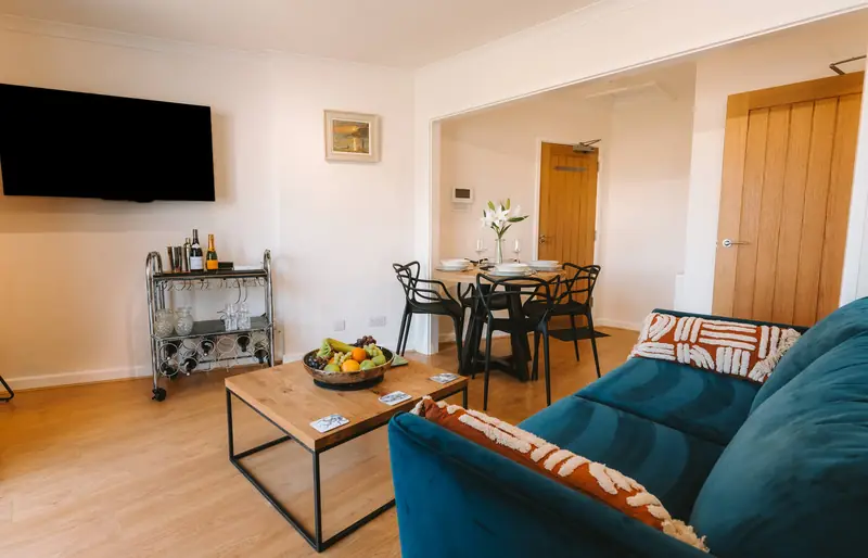 Open-plan living room with teal sofa, TV and dining table